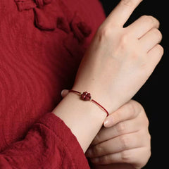 Cinnabar four leaf clover bracelet worn on model wrist with matching red traditional garment against black background showing carved red charm and gold accent beads