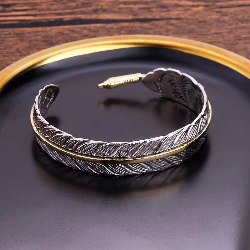 Silver and gold feather cuff bracelet with oxidized finish, etched feather barb details and gold terminal accents on black gold-rimmed tray