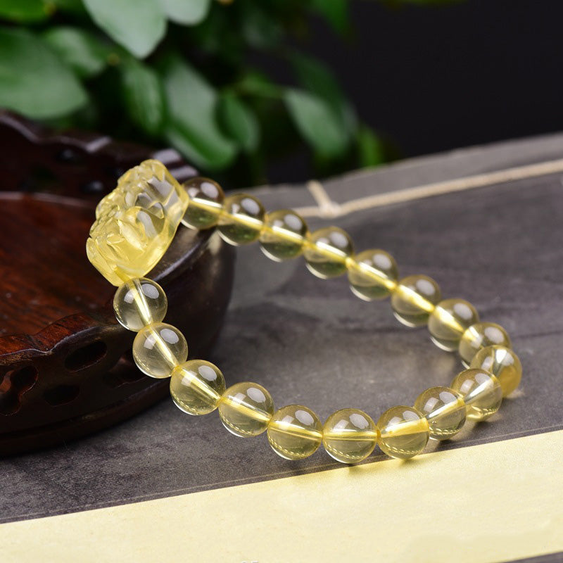 Citrine PiXiu Wealth Bracelet – PiXiu facing left on dark book with green foliage background, citrine prosperity jewelry
