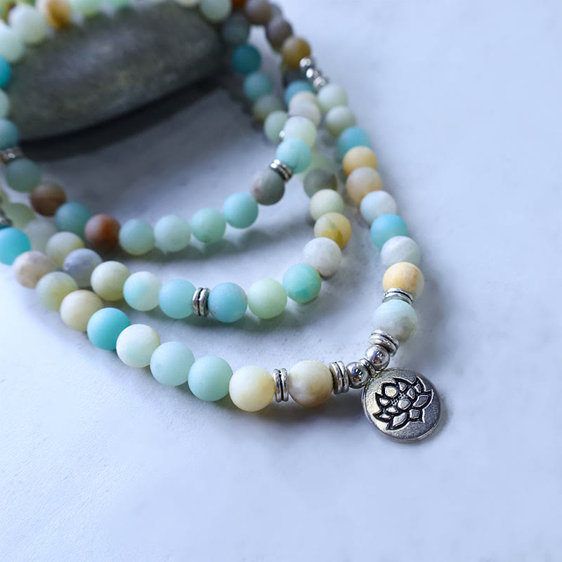 Amazonite Lotus Mala – bracelet in S-curve near pebble with lotus charm in focus, amazonite