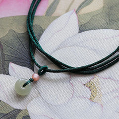 Jade Peace Buckle Lotus Necklace – Flat lay of jade donut on green cord with knot on lotus printed fabric, jade necklace