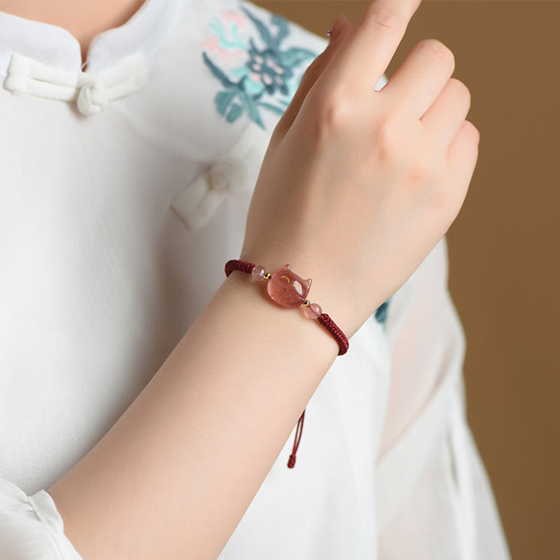 Pink strawberry quartz cat bracelet with burgundy braided cord worn on woman's wrist, adjustable handmade cat protection jewelry