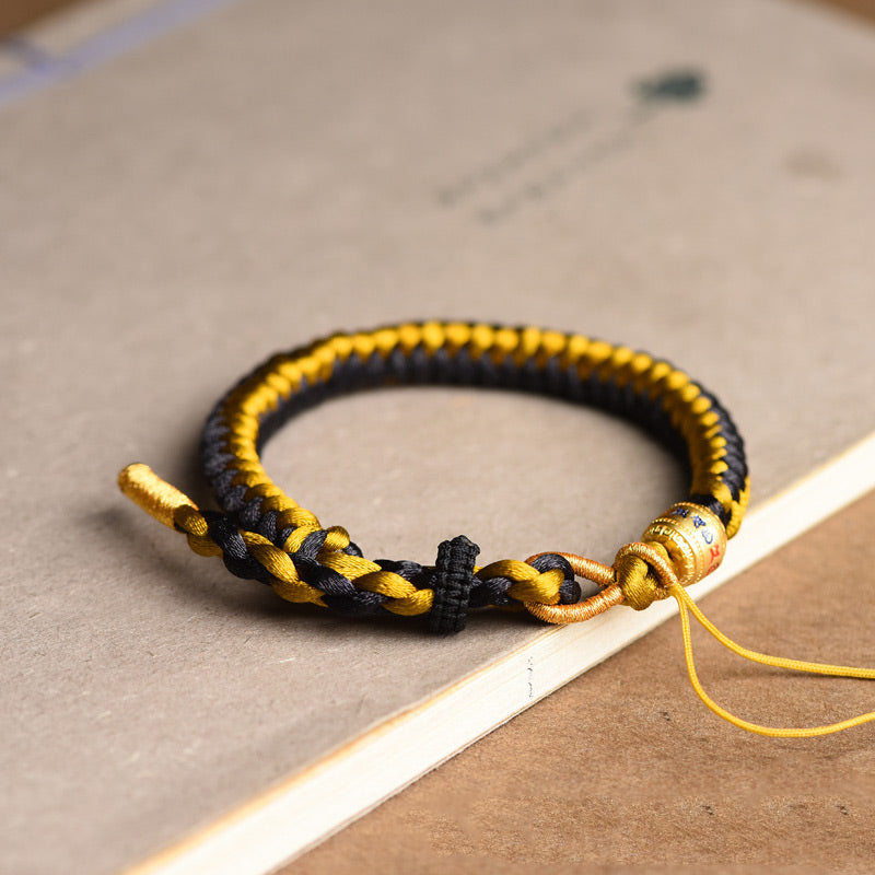 Tibetan Black Gold Dragon Scale Bracelet – relaxed arc on tan kraft paper, gold charm detail, woven cord bracelet