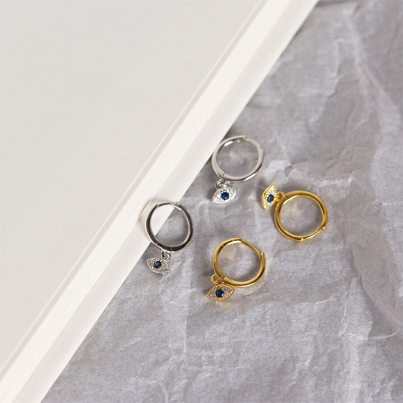Silver & Gold Evil Eye Huggie Earrings with Crystals on Gray Textured Paper Surface