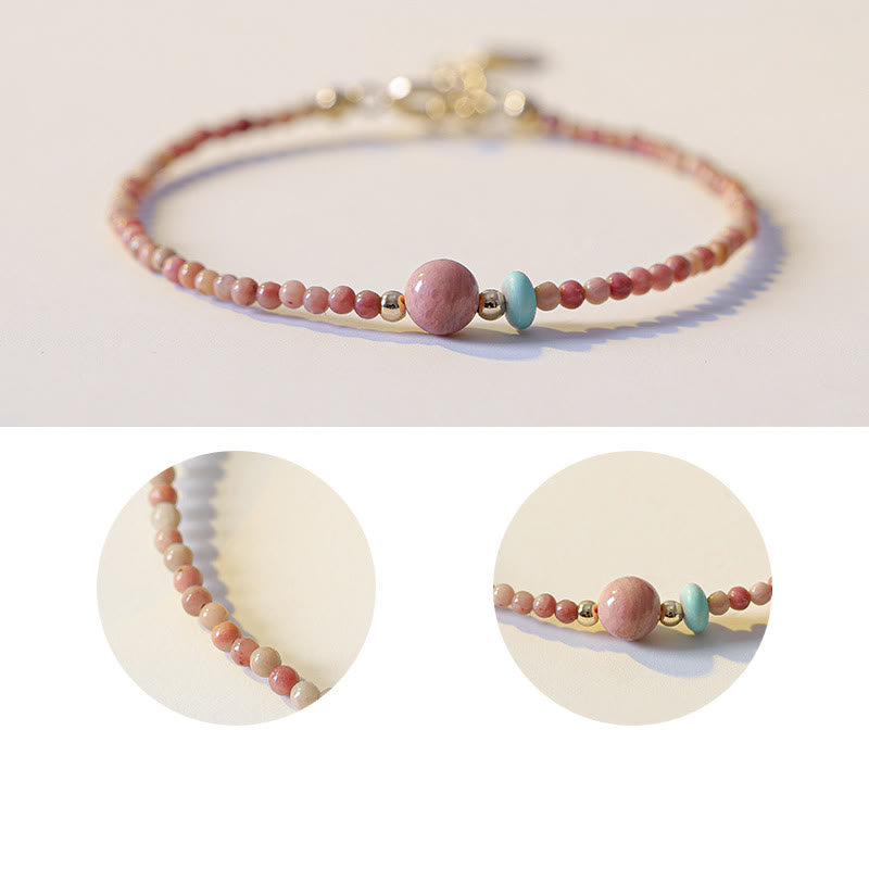 Rhodonite Loving Energy Bracelet – Coral-pink beads with pink focal, turquoise accent and gold spacers on cream off-white surface, low side perspective