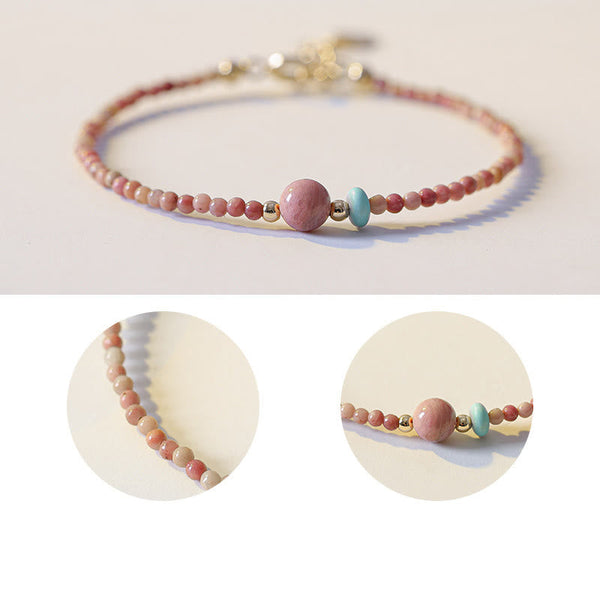 Rhodonite Loving Energy Bracelet – Coral-pink beads with pink focal, turquoise accent and gold spacers on cream off-white surface, low side perspective