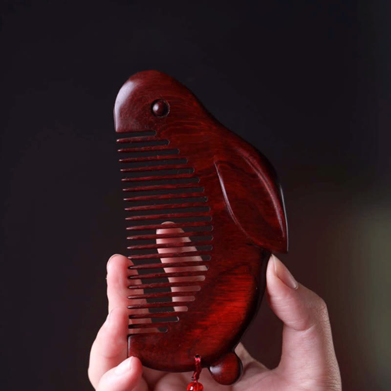 Hand holding red sandalwood bunny comb against dark background