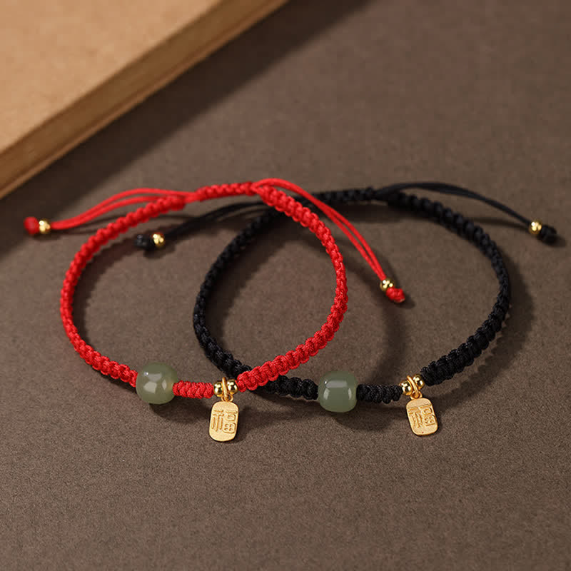 Pair of 925 silver Hetian jade red string bracelets showing red cord and black cord options with green jade bead and gold fu fortune character charm on textured brown surface