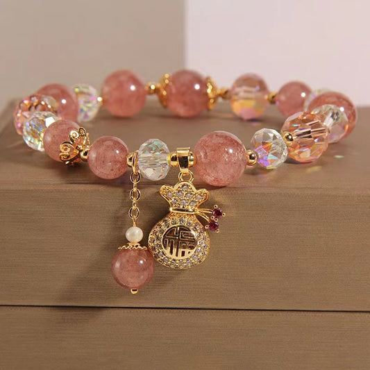 Strawberry quartz money bag fu charm bracelet with pink crystal beads AB aurora crystal accents gold-toned money bag pendant with pave crystals and Chinese fu character blessing symbol on wooden surface