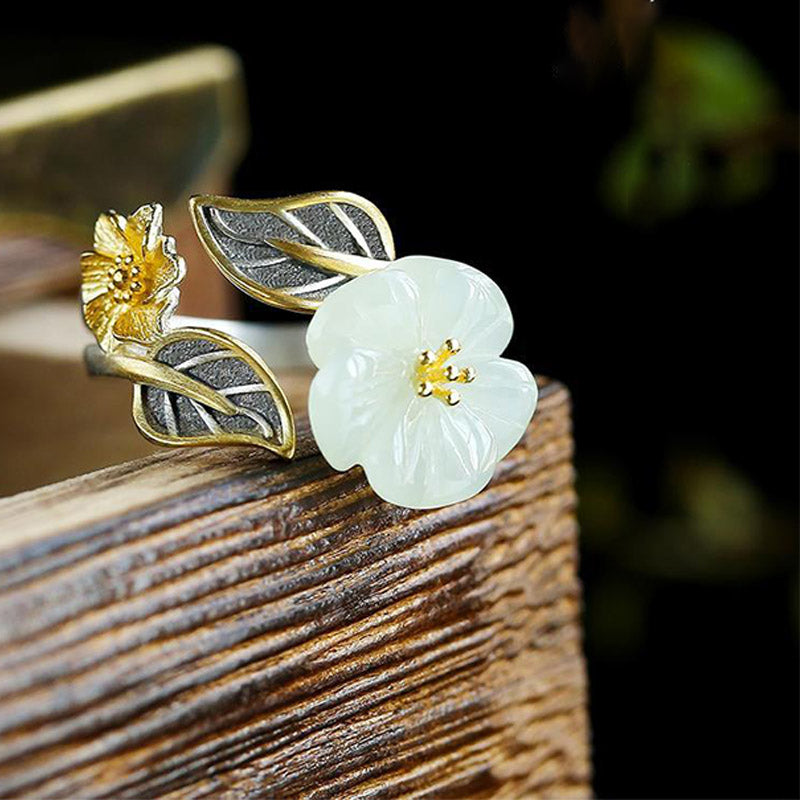 White Jade Plum Blossom Silver Ring - Floral ring on rustic wood showing five-petaled jade blossom, gold-tone stamen details, and two-tone silver-gold leaf accents