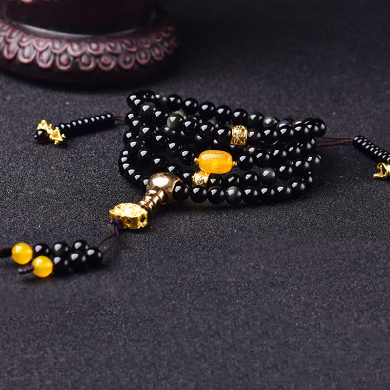 Black Obsidian Lotus Mala Bracelet - Diagonal coil on dark fabric, amber accent and gold metalwork, obsidian