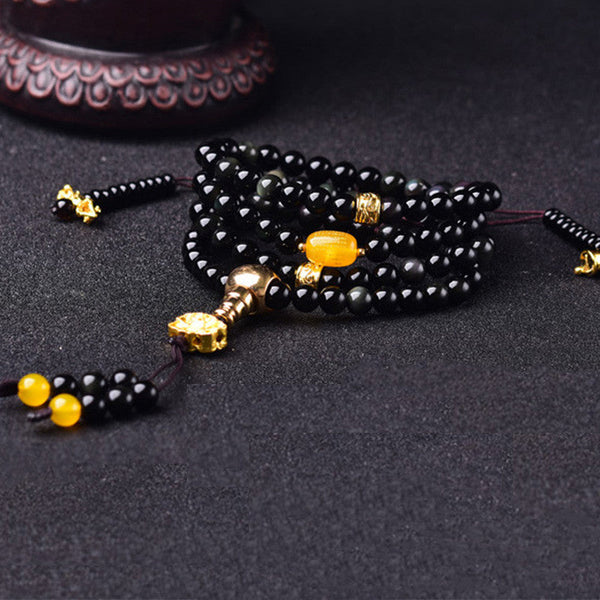 Black Obsidian Lotus Mala Bracelet - Diagonal coil on dark fabric, amber accent and gold metalwork, obsidian