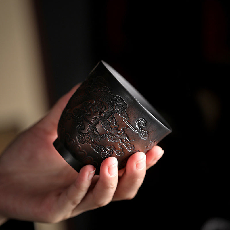 Ceramic Tea Cup – Hand cradling dragon and cloud relief, close-up of carved dark clay