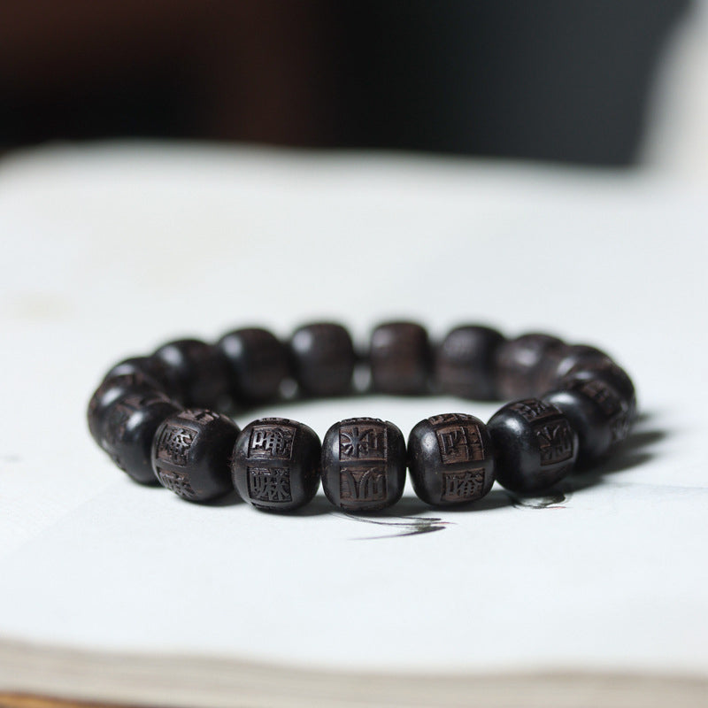 Ebony Wood Mantra Bracelet – Side angle of carved beads with dark bokeh background, engraved wood