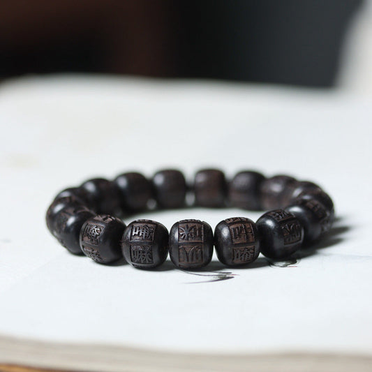 Ebony Wood Mantra Bracelet – Side angle of carved beads with dark bokeh background, engraved wood