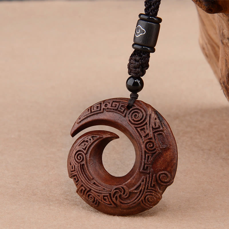 Red sandalwood peace buckle spiral pendant necklace with traditional Chinese cloud scroll carving on warm brown wood disc suspended from black braided cord with silver cloud inlay bead