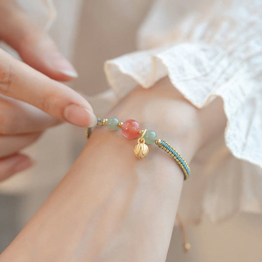 Red Agate Jade Lotus Bracelet – blue gold woven cord with coral and jade beads, lotus charm, white lace sleeve lifestyle photo