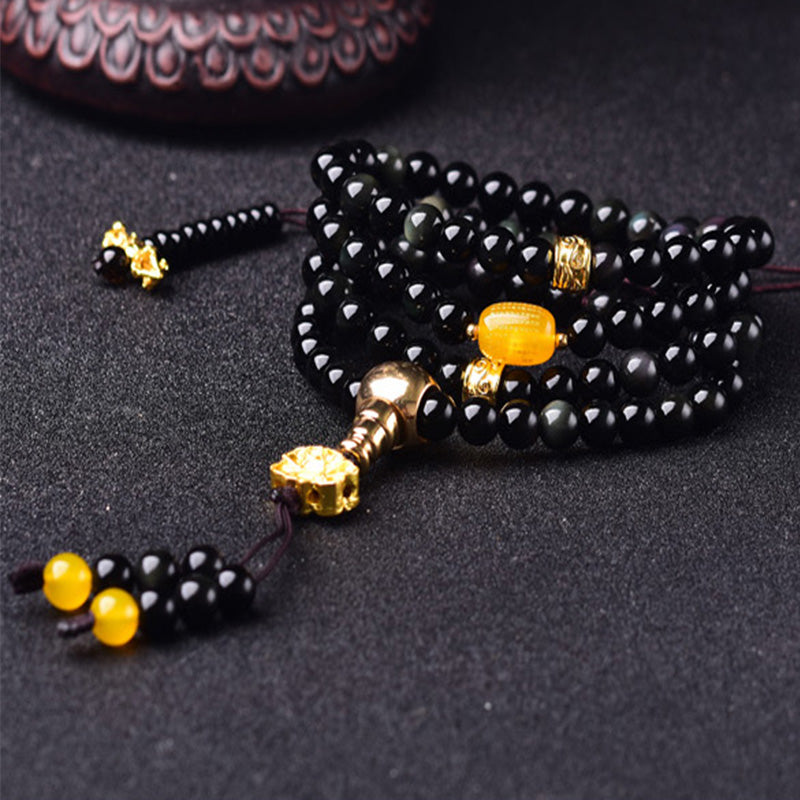 Black Obsidian Lotus Mala Bracelet - Low angle on charcoal with wood prop, gold stupa guru bead, obsidian