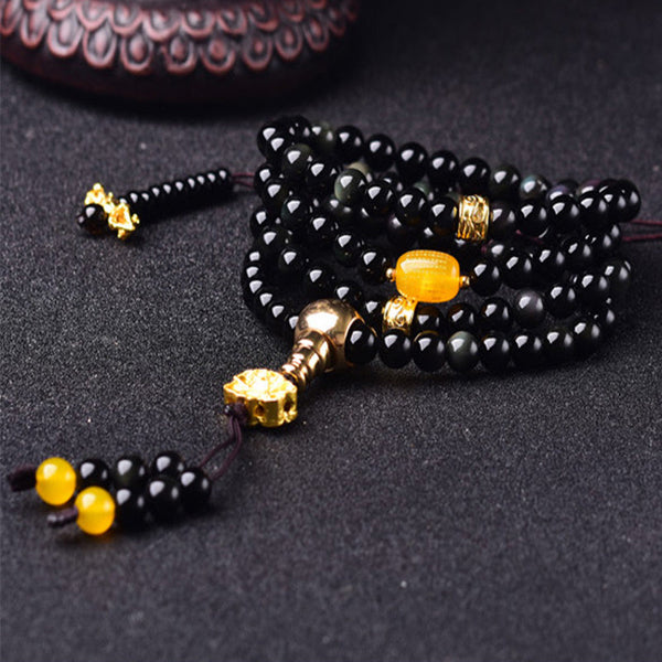 Black Obsidian Lotus Mala Bracelet - Low angle on charcoal with wood prop, gold stupa guru bead, obsidian