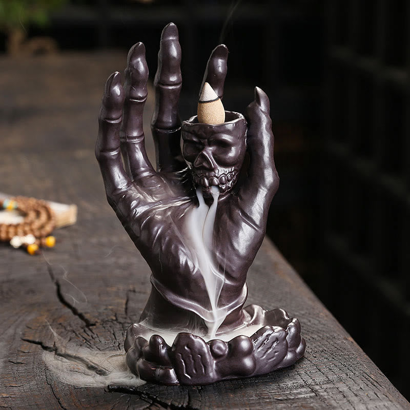 Ceramic Ghost Hand Skull Incense Burner – Skeletal hand cradling skull with smoke cascading on dark wood, backflow incense burner Hauptbild