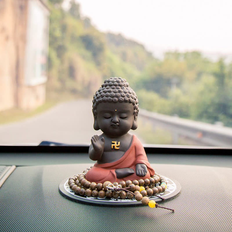 Small Buddha Purple Clay Decoration – placed on car dashboard with rural road bokeh, mala beads around base, travel blessing