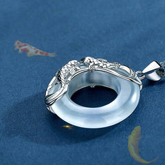 Elegant silver koi fish necklace featuring white jade donut pendant in ornate setting with detailed fish sculpture, koi pond background