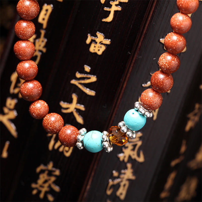 Goldstone Mala Bracelet – beaded bracelet on calligraphy wood surface, turquoise and goldstone