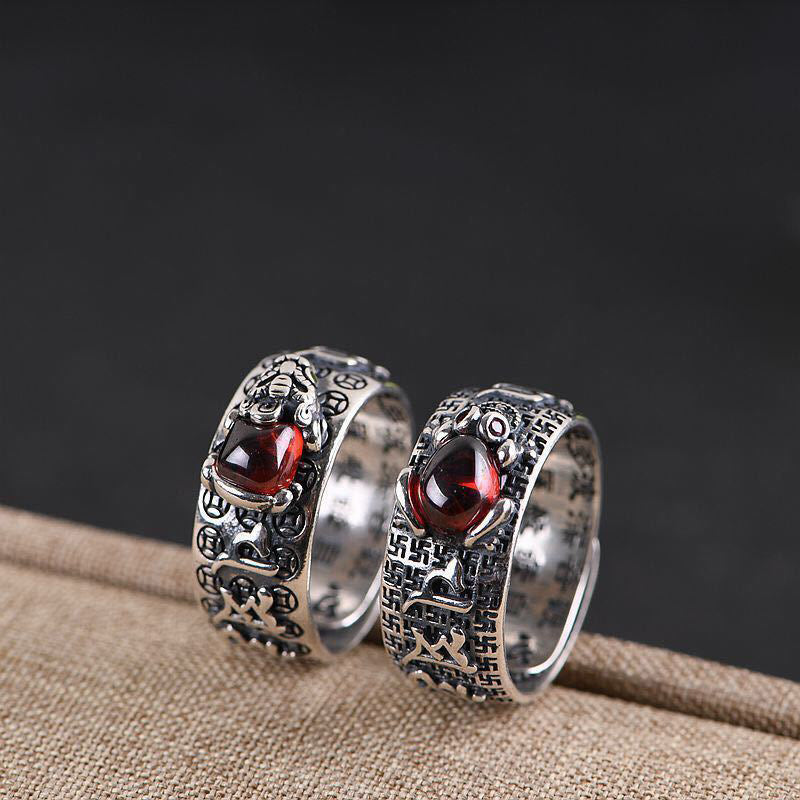 Feng Shui PiXiu Ring – Pair of silver rings with red stones on burlap against dark backdrop