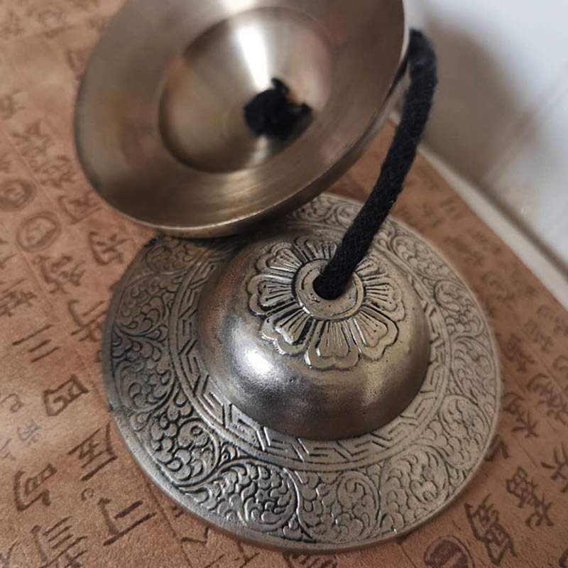Tibetan Tingsha Bells – Close-up lotus mandala and cloud motif engravings on script background, singing cymbals