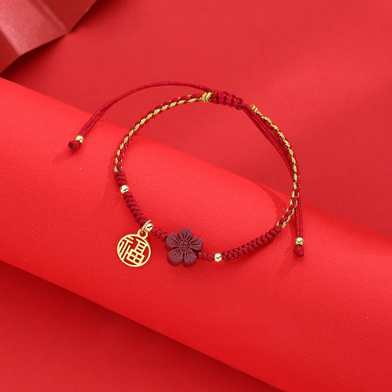Adjustable red string bracelet with gold Fu fortune charm and cinnabar flower pendant, traditional Chinese lucky knot cord jewelry on red backdrop