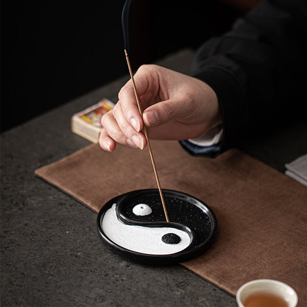 Yin Yang Incense Holder – Hand lighting incense stick in zen tray with tea cup nearby, Mindful