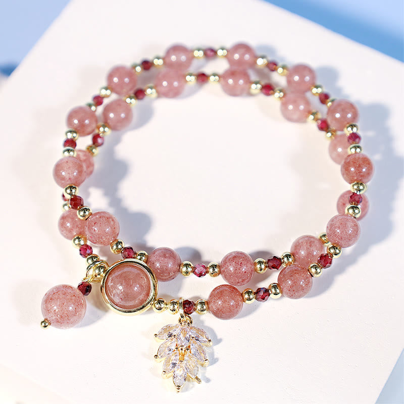 Double-strand strawberry quartz bracelet coiled on white surface showing alternating pink beads and burgundy accents gold spacers clear crystal leaf pendant and teardrop charm