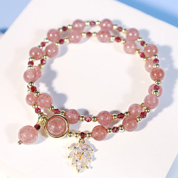 Double-strand strawberry quartz bracelet coiled on white surface showing alternating pink beads and burgundy accents gold spacers clear crystal leaf pendant and teardrop charm