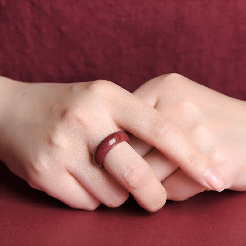 Cinnabar Om Mani Padme Hum Blessing Ring – deep burgundy cinnabar band worn on clasped hands, matching fabric, lifestyle close-up
