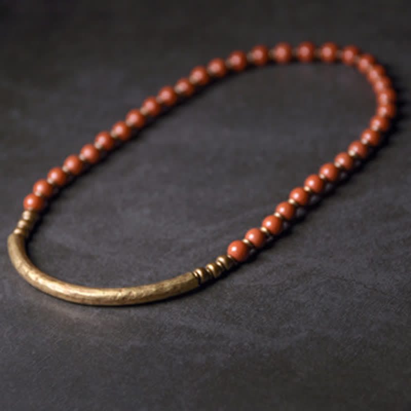 Red jasper and antique bronze bar bracelet in relaxed oval shape, warm terracotta beads with aged gold metal tube centerpiece on dark background