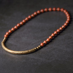 Red jasper and antique bronze bar bracelet in relaxed oval shape, warm terracotta beads with aged gold metal tube centerpiece on dark background