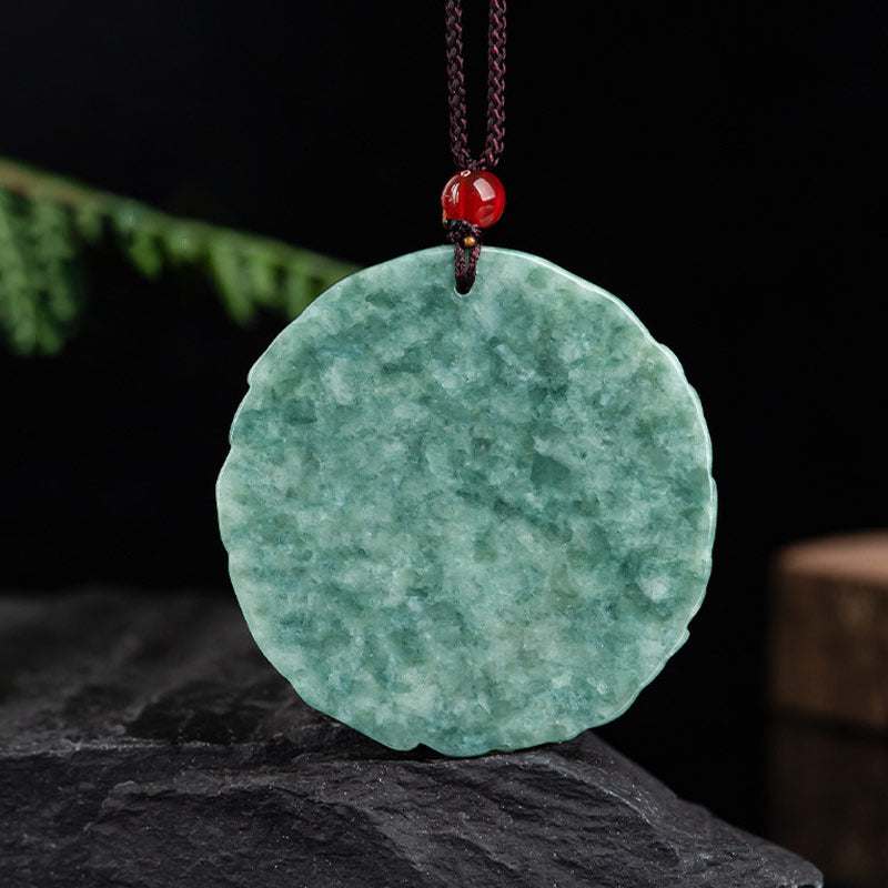 Dragon Jade Yin Yang Necklace – Green jade disc with faint scalloped edge on dark cord, dark reflective stone surface with green foliage, frontal