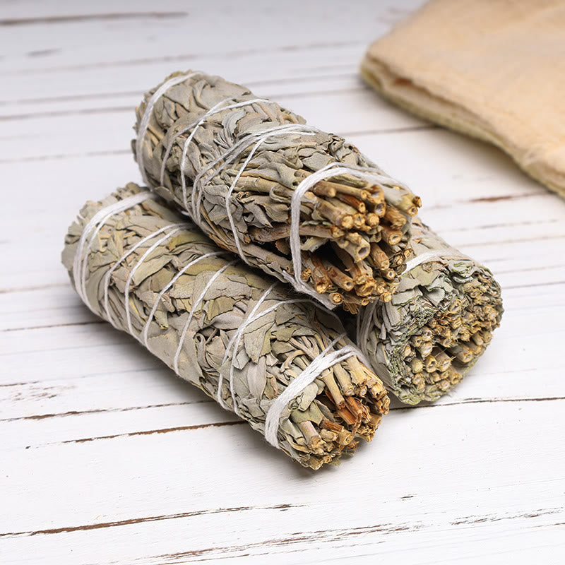 Three white sage smudge sticks bundled with cotton string on whitewashed wood