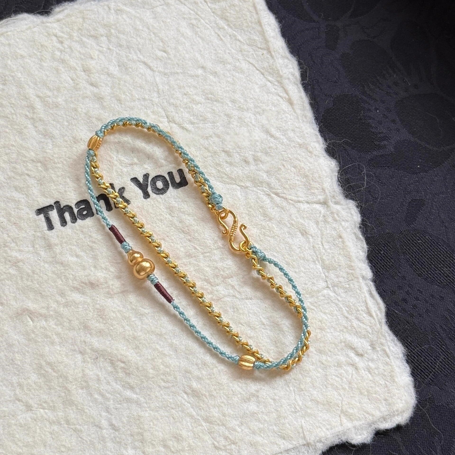 Double-Layer Gourd Bracelet – Close-up of gold chain links and cord ends with beads on white felt, protection