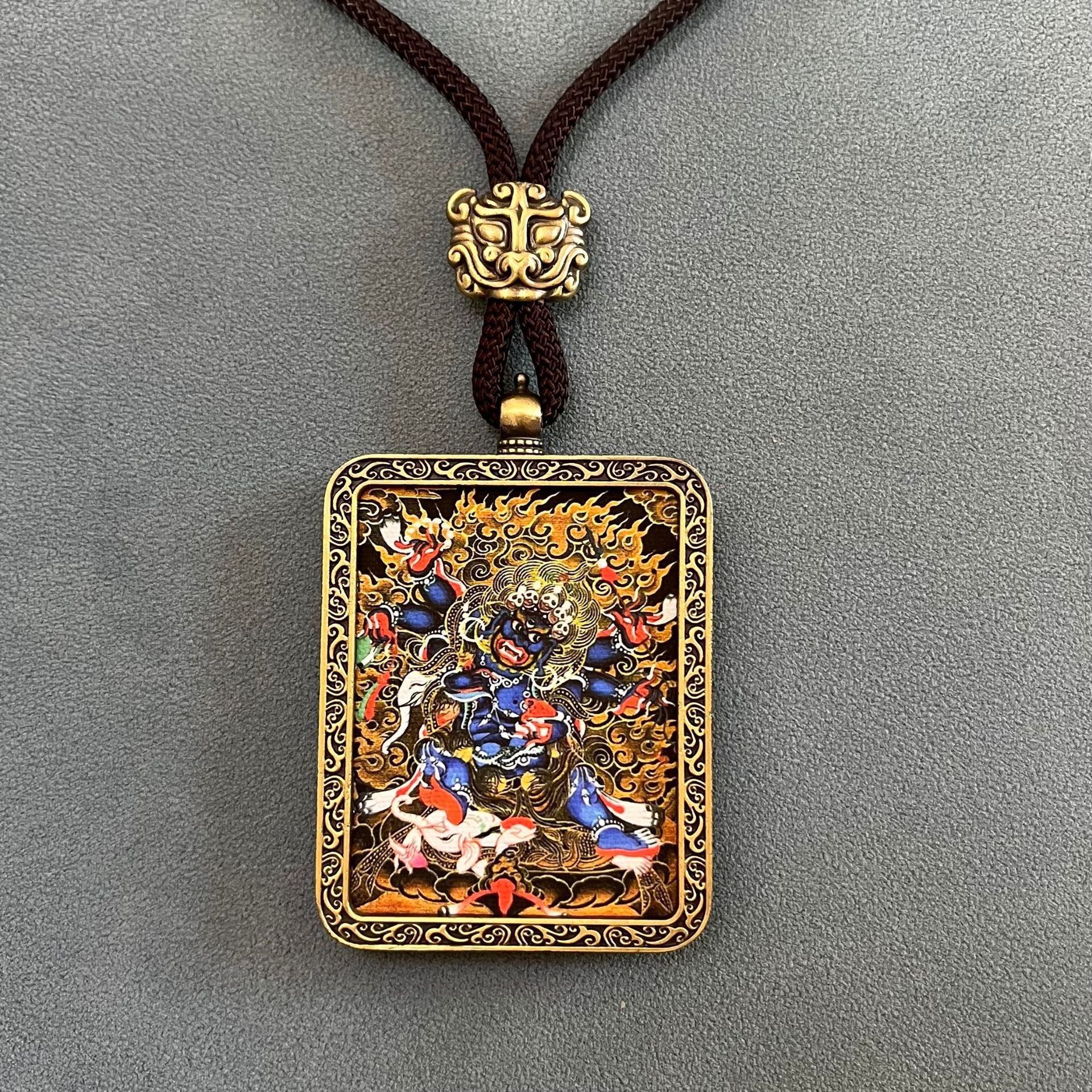 Tibetan Thangka Pendant – front-facing blue deity thangka in gold casing, brown braided necklace, Buddhist wealth blessing