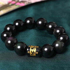 Rainbow Obsidian Bracelet – Close-up of glossy black beads with gold mantra charm on teal fabric, obsidian jewelry