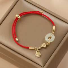 Chinese red cord bracelet with pale green jade peace buckle, gold key charm with crystal accent and fortune lock pendant in beige velvet jewelry box