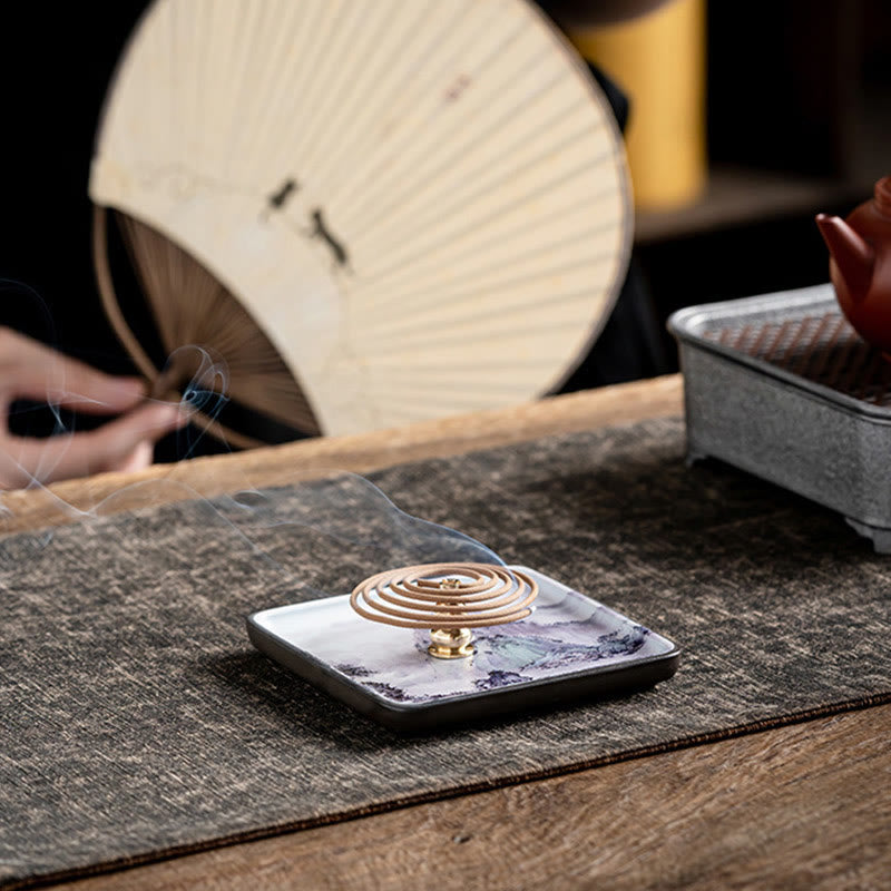 Coil Incense Burner – Spiral incense smoking on purple mountain ceramic plate with tea fan and teapot