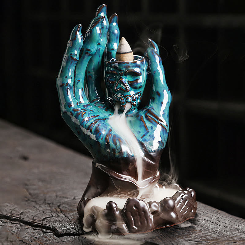 Ceramic Ghost Hand Skull Incense Burner – Iridescent turquoise hand skull with backflow cone lit, smoke cascading on wood
