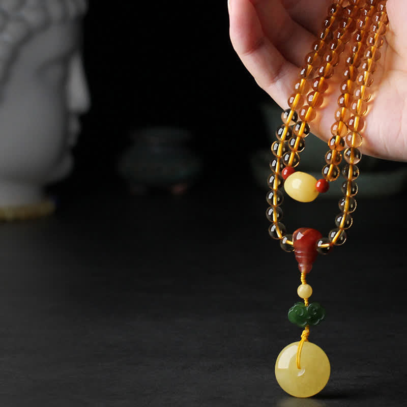 Citrine Mala Bracelet – Hand holding citrine bead necklace with amber peace buckle, dark bg