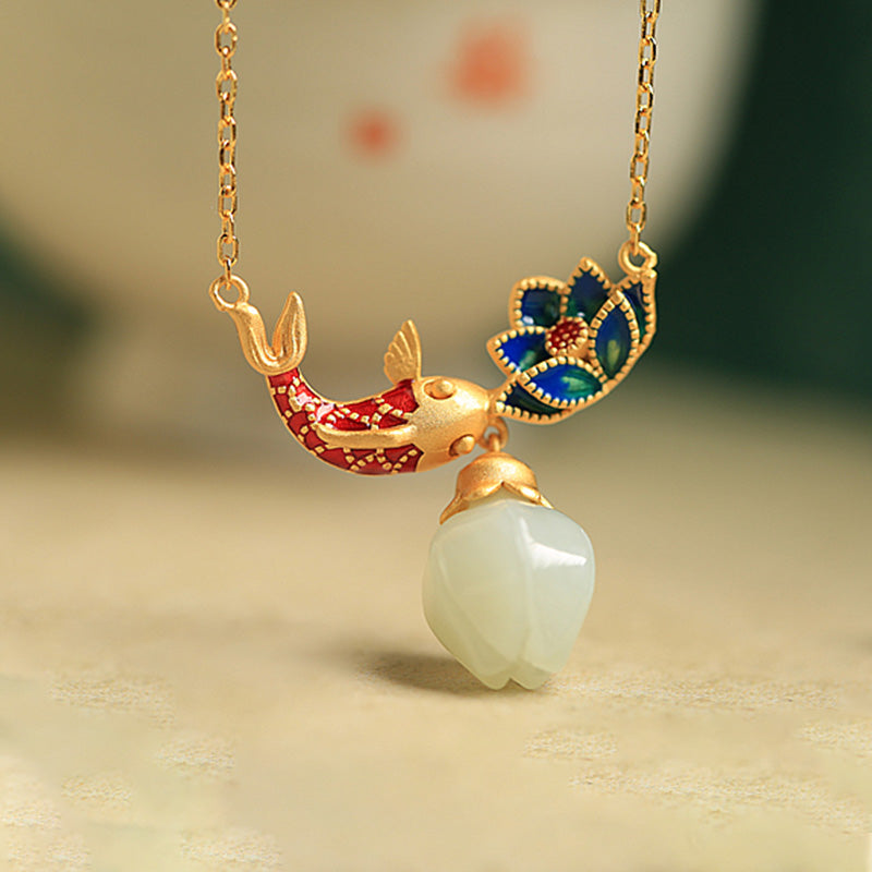 White Jade Koi Fish Necklace – macro close-up of red enamel koi with blue lotus and carved jade bud on cream surface