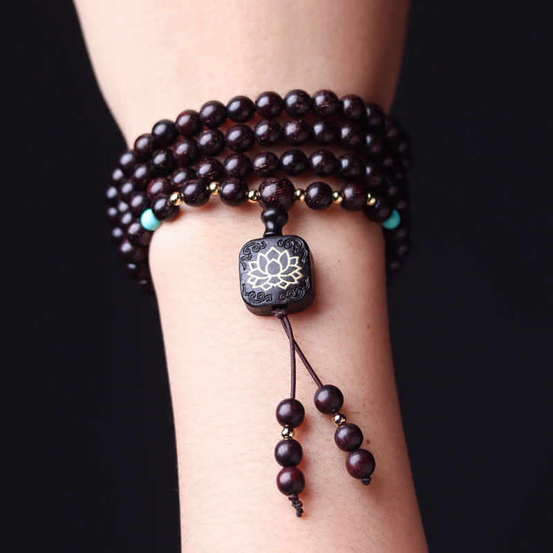 Red sandalwood 108 bead mala bracelet wrapped around wrist multiple times with turquoise markers, gold spacers and silver lotus inlay guru bead on black background