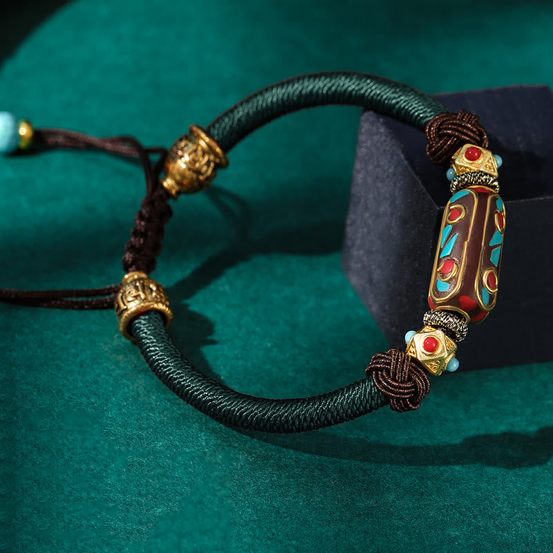Tibetan Turquoise Om Mani Padme Hum Braided Bracelet – Dark teal cord variant with gold accents on green velvet display