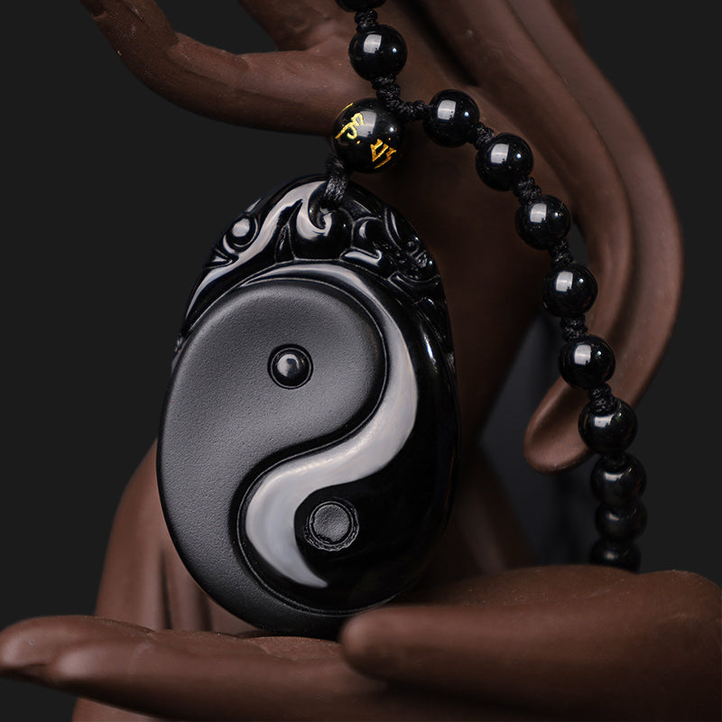 Black Obsidian Yin Yang Pendant Necklace – Polished obsidian Yin-Yang amulet on ceramic display, carved stone jewelry