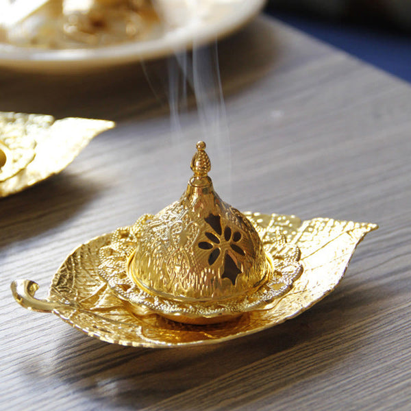 Tibetan Gold Leaf Coaster Incense Burner – Gold dome with smoke rising from floral cutouts on wooden surface, brass incense holder